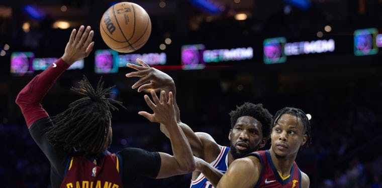 Joel Embiid (21 in blue) looks to pass out of a Cavaliers double team in a 2022 NBA game inside Wells Fargo Center. 