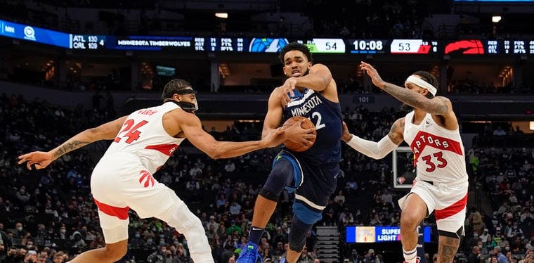 Minnesota Timberwolves center Karl-Anthony Towns (32) drives to the basket against Toronto Raptors Khem Birch (24) and guard Gary Trent Jr. (33) in a game in Minneapolis.